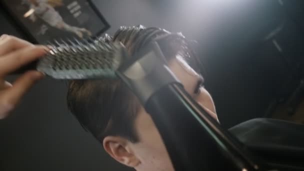 Парикмахер укладывает волосы своего клиента на висках феном и расчёской — стоковое видео