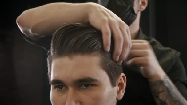 Frisör i svart mask styla sin klient hår med hjälp av en gel — Stockvideo