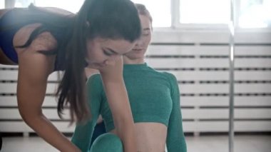 Doing yoga in fitness studio - trainer correcting posture of her students