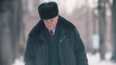 An old man walking in the park while snowfall