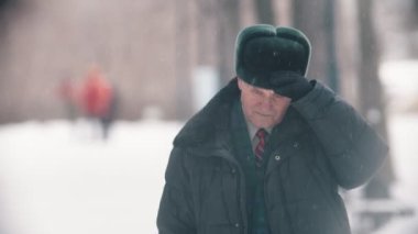 An old man takes off his hat and cleaning it up from the snow