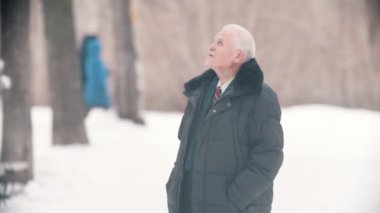 An old man veteran with grey rare hair walking in the snowy park while snowfall
