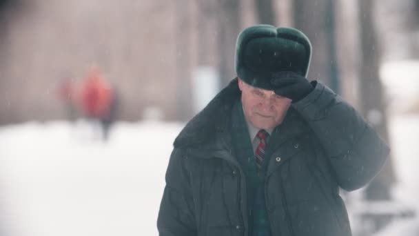 Um velho tira o chapéu e limpa-o da neve. — Vídeo de Stock