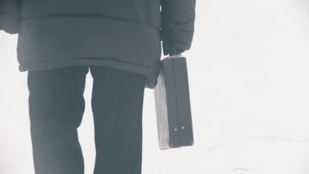 An elderly man in down jacket with bag walking in the snowy park — Stock video