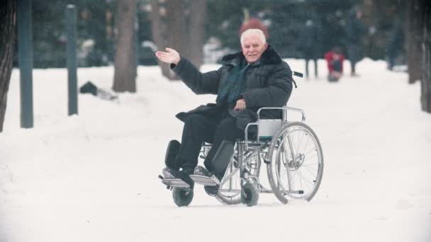 Старик ветеран, сидящий в инвалидном кресле и машущий рукой в камеру — стоковое видео