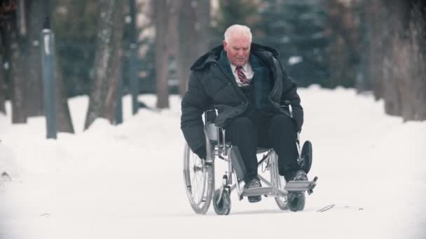 An old man veteran sitting in a wheelchair under the snowfall — 图库视频影像