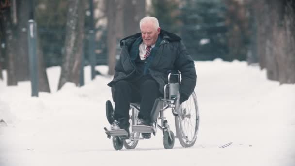 An old man veteran in a wheelchair trying to move on the snowy ground — Stockvideo