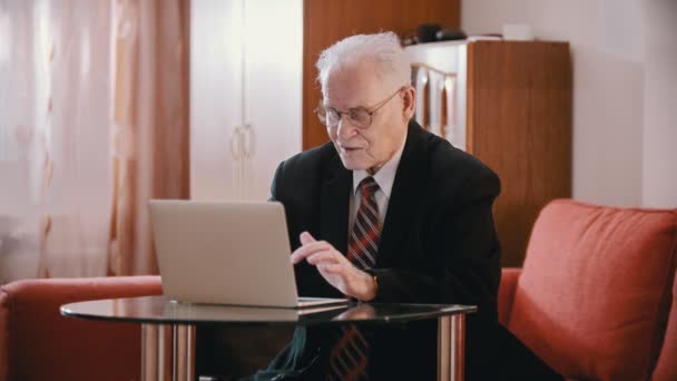 Abuelo anciano - abuelo viejo con gafas está escribiendo en un ordenador — Vídeos de Stock