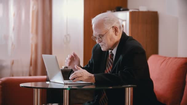 Літній дід - старий дідусь поступово щось пише на комп'ютері в кімнаті — стокове відео