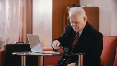 Elderly grandfather - old grandfather is putting glasses on the table and taking out a gun