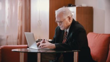 Elderly grandfather - old grandfather in a suit is typing something on a computer and taking off his glasses tiredly