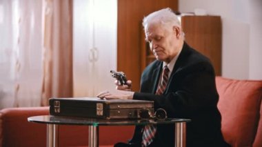 Elderly grandfather - old grandfather is taking a gun out of a suitcase, charging it and pointing it at the camera
