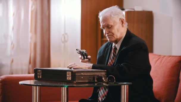 Elderly grandfather - old grandfather is taking a gun out of a suitcase, charging it and pointing it at the camera — Stock Video