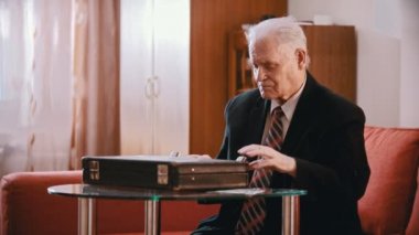 Elderly grandfather - the old grandfather is taking money from a suitcase and putting it on the table, then taking out a gun and putting it on a suitcase