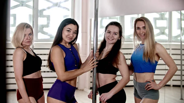Четыре спортивные женщины, стоящие у столба для танцев на шесте в студии — стоковое фото