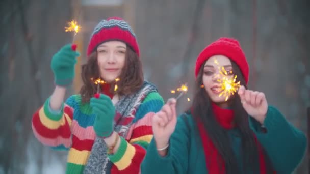 Dos jóvenes mujeres sonrientes bailando al aire libre en invierno con bengalas encendidas — Vídeo de stock