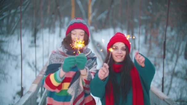 Zwei junge lächelnde Frauen spielen mit Wunderkerzen und blicken in die Kamera — Stockvideo