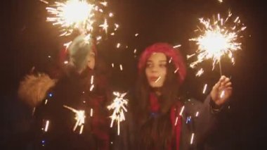 Two young smiling women playing with sparklers at night and looking in the camera