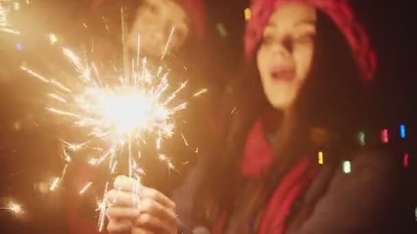 Две девушки-подружки, играющие ночью с бенгальскими огнями и поющие песню - смотрят в камеру — стоковое видео