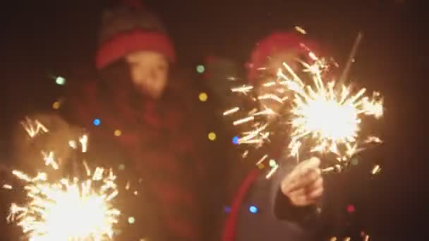 Two young smiling women friends playing with sparklers at night and dancing - looking in the camera — Stock video