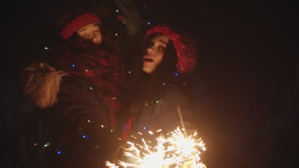 Duas jovens amigas brincando com faíscas à noite e dançando olhando para a câmera — Vídeo de Stock