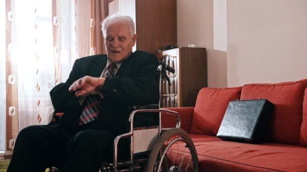 Elderly grandfather - grandfather is sitting in a wheelchair and checking the time on a wristwatch — Stockvideo