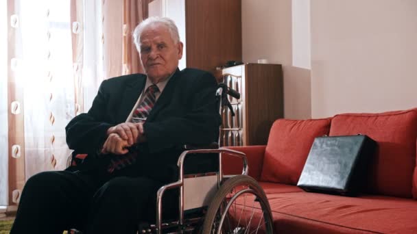 Дід похилого віку - дід сидить у інвалідному візку і натирає руки — стокове відео