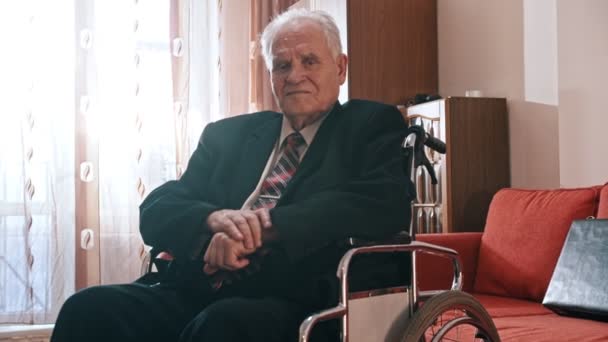Anciano abuelo - abuelo está sentado en una silla de ruedas, levanta la manga de su chaqueta y mirando el reloj — Vídeo de stock