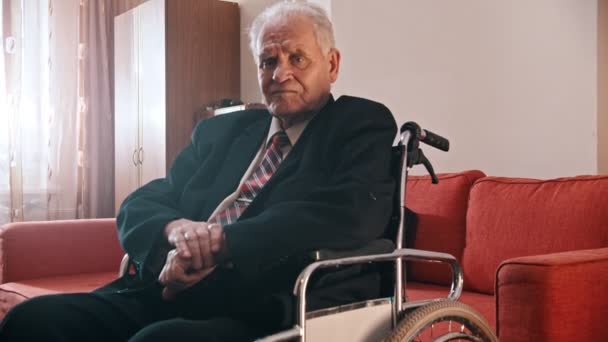 Elderly grandfather - sad grandfather is sitting in a wheelchair and looking at the camera — Wideo stockowe