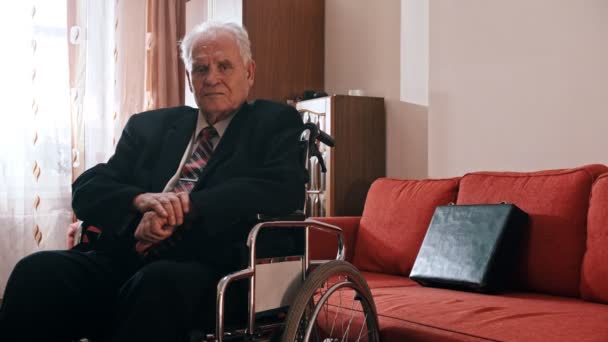 Elderly grandfather - sad grandfather is sitting in a wheelchair in his room and looking at the camera — Stockvideo