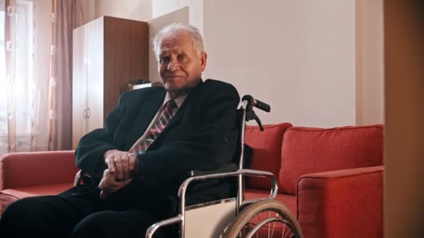 Пожилой дедушка - счастливый дедушка сидит в инвалидном кресле и смотрит в камеру — стоковое видео
