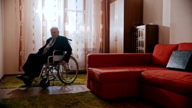 Yaşlı büyükbaba, büyükbaba tekerlekli sandalyesiyle odada dolaşıyor.