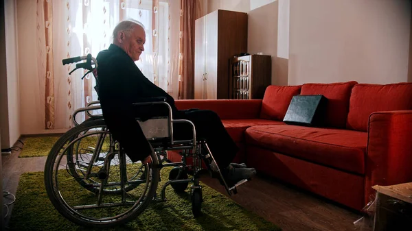 An old man sitting in a wheelchair in the room — Stock Photo, Image