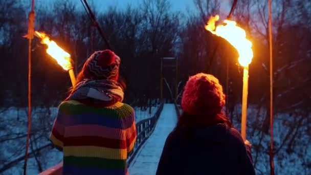 Две юные подруги идут по мосту, держа факелы вечером. — стоковое видео