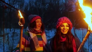 İki genç, gülümseyen kadın arkadaş, gece köprüde ellerinde meşalelerle durup etrafa bakınıyorlar.