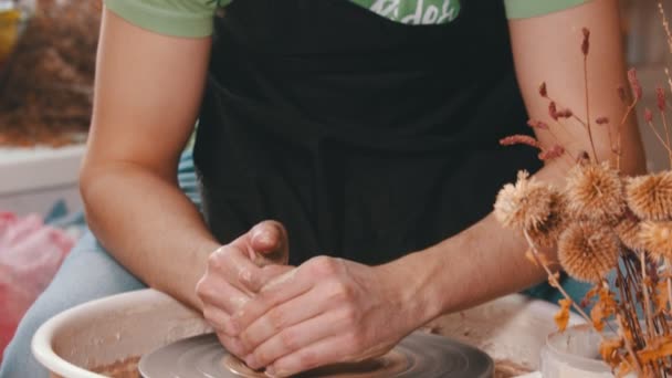 Pottery - mistr v zeleném tričku se dvěma rukama stlačuje hlínu na hrnčířském kole — Stock video