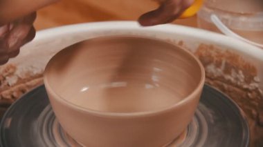 Çanak çömlek. Adam kasenin altını sarı bir süngerle siliyor.