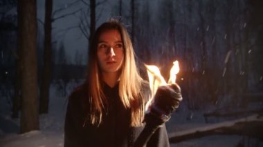 Kış ormanında kar altında meşale tutan genç bir kadın.