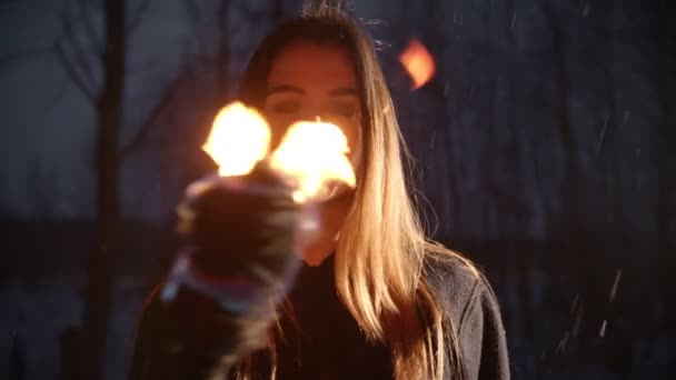 Young woman with torch standing in winter forest under the snowfall and looking in the camera — Αρχείο Βίντεο