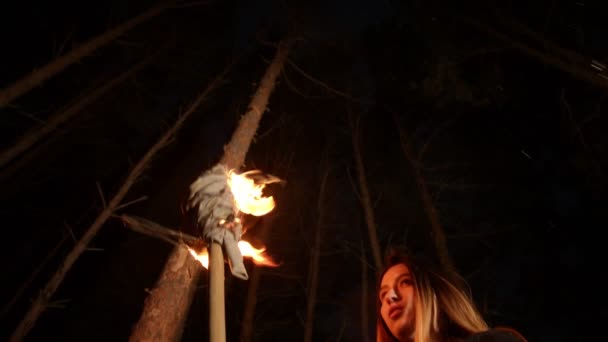 Jeune femme perdue debout dans la forêt d'hiver la nuit avec une torche à la main 