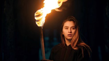 Young beautiful woman with fired torch in night forest looking to the side
