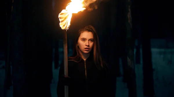 Young woman with fired torch in night forest looking in the camera