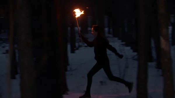Молодая женщина с факелом убегает от чего-то в ночном лесу — стоковое фото