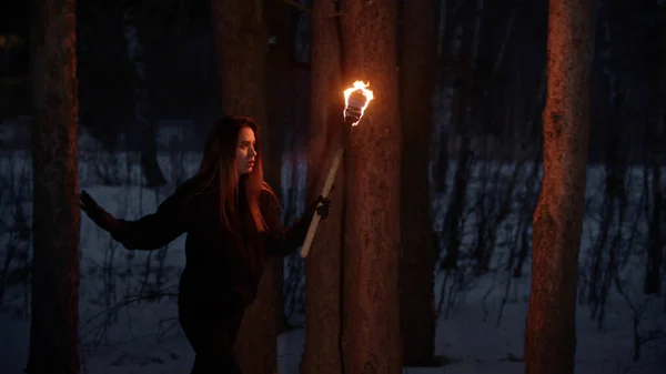 Young lost woman with torch walking in the night winter forest