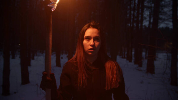 Young woman with long hair walking in the night forest holding a handmade torch