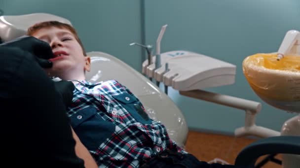 Маленький нервный мальчик полирует зубы в стоматологии и выплевывает воду — стоковое видео