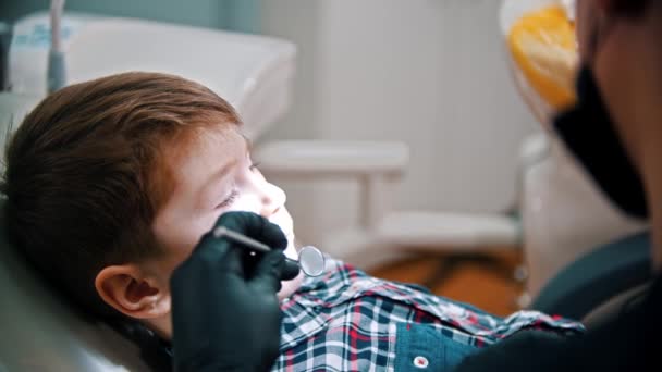 Um dentista examina a boca de um menino na odontologia — Vídeo de Stock