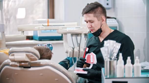 Joven dentista mostrando un modelo plástico de mandíbulas humanas a un niño pequeño — Vídeo de stock