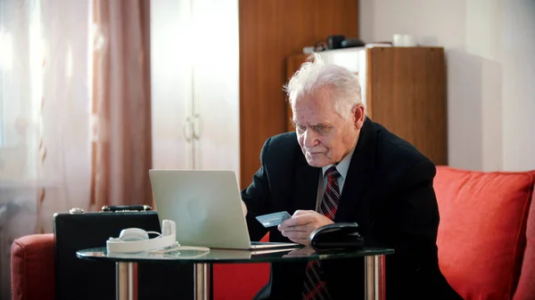 Elderly grandfather - old grandfather is entering bank card number into laptop — Stockfoto