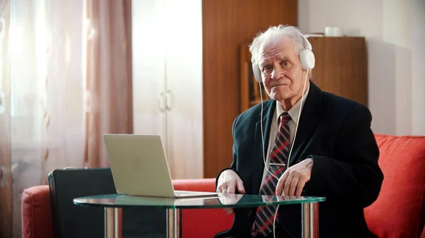 An old man in headphones sitting by the laptop — Stock Photo, Image